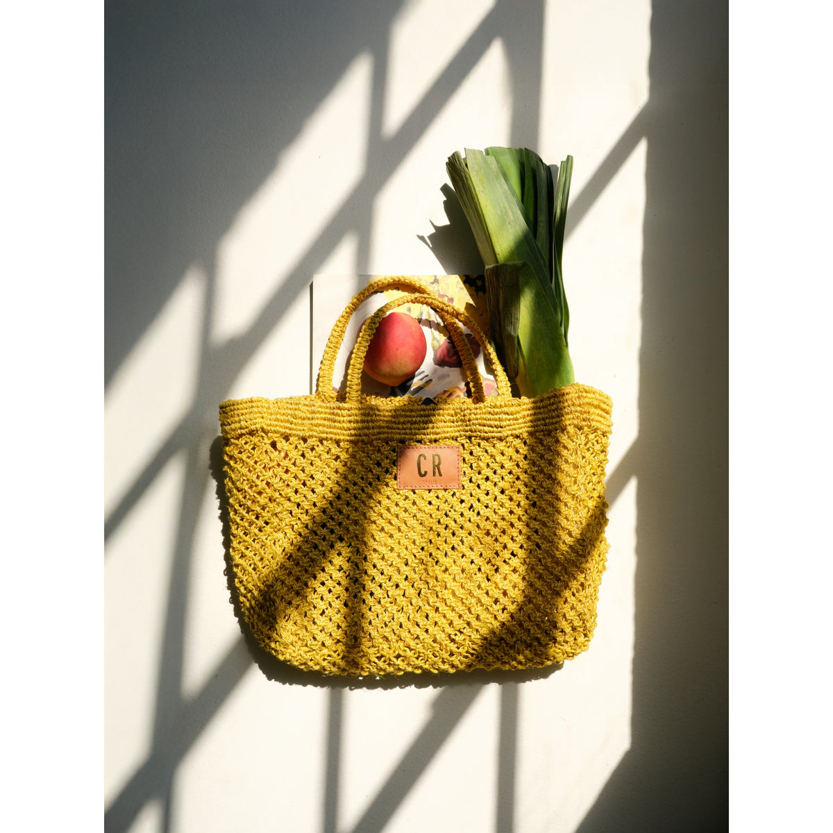 Petite Mercado Tote in Ocre — photographed against a sunlit wall, filled with leeks and fruit from a market run