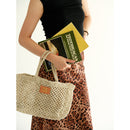 Petite Mercado in Natural — close view of the front of the bag and its leather patch as it is carried by hand with a book