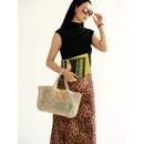 Petite Mercado in Natural — carried in hand alongside a book, with the leather patch facing the camera