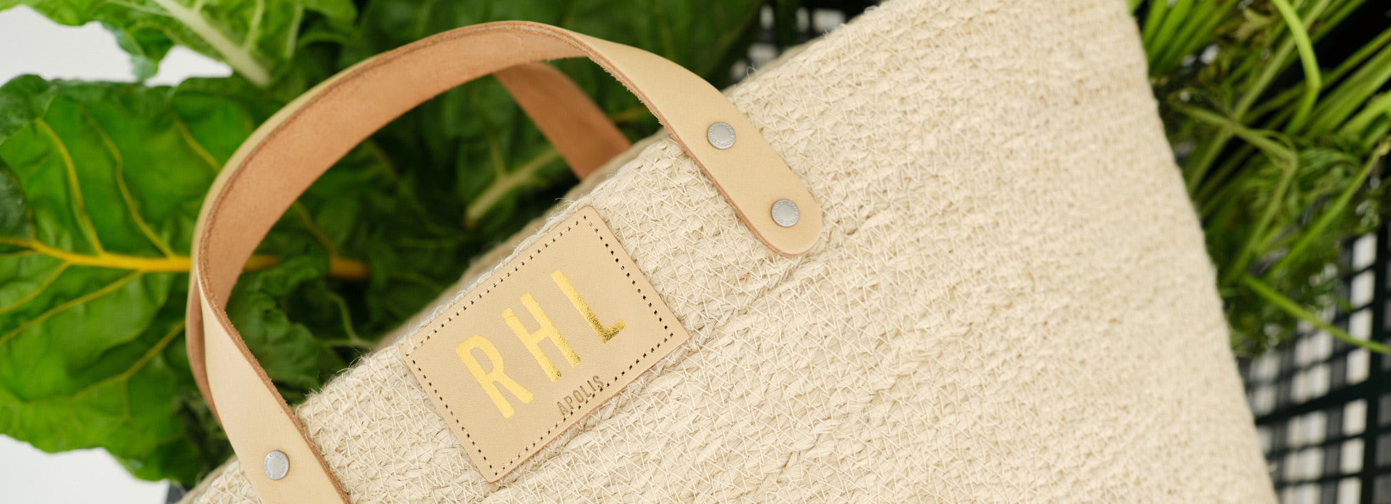 Apolis bag with gold monogram among green leaves